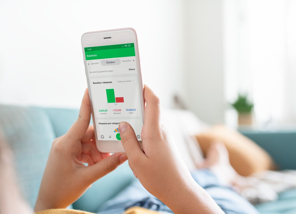 Mão segurando smartphone com aplicativo de controle financeiro mostrando gráficos de gastos